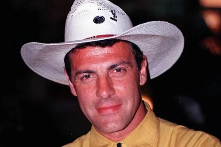 Gerson Brenner sorrindo, usando um chapéu de cowboy branco com detalhes em metal e uma camisa amarela.