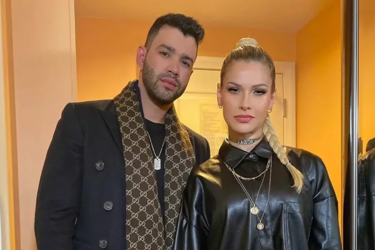 Gusttavo Lima e Andressa Suita posam juntos; ele veste sobretudo preto com cachecol marrom da Gucci e ela usa camisa de couro preta com trança lateral loira.
