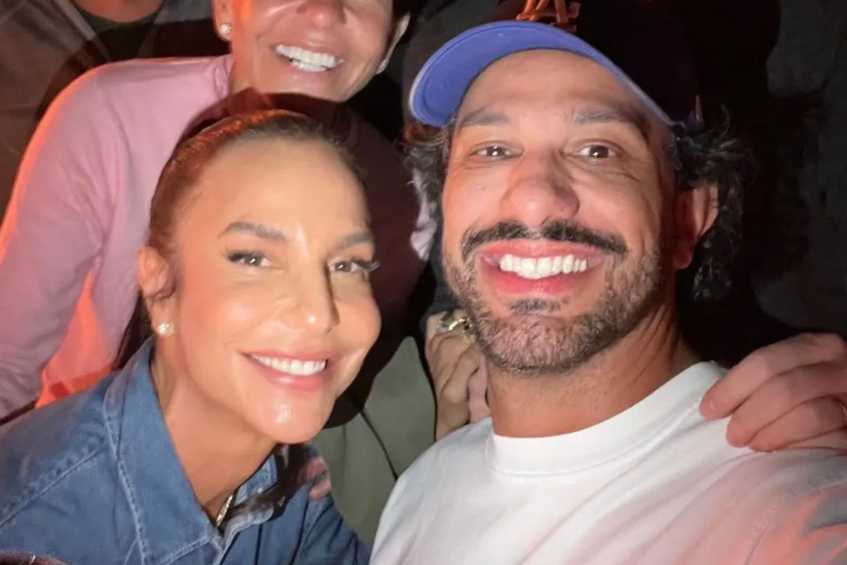 Ivete Sangalo sorri ao lado do empresário Tiago Maia em selfie aproximada. Ela usa camisa jeans e ele veste camiseta branca e boné azul.