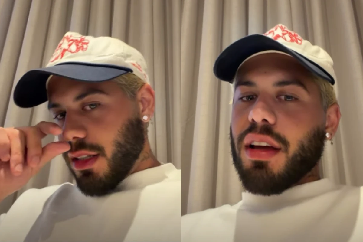 Cantor Zé Felipe com cabelo loiro platinado e barba aparada, usando um boné branco com aba azul e detalhe bordado em vermelho, vestindo uma camiseta branca, em um ambiente interno com cortinas claras ao fundo.