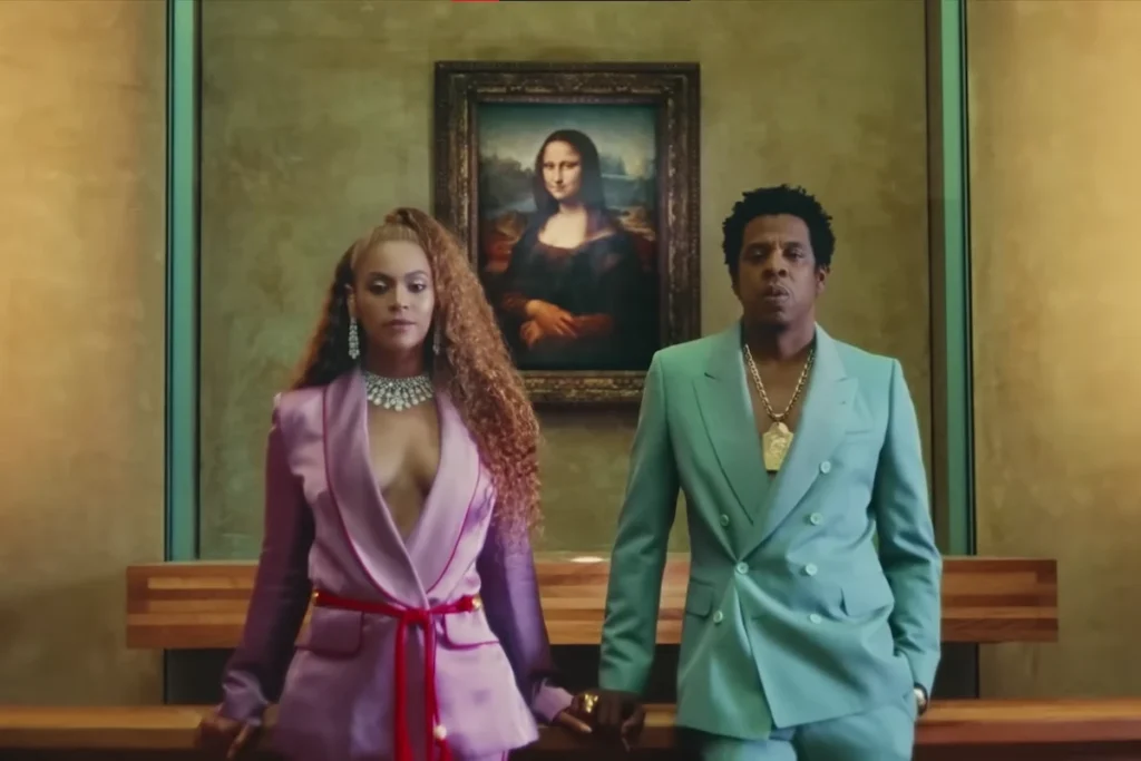 Beyoncé e Jay-Z posam lado a lado em frente ao quadro da Mona Lisa no Museu do Louvre. Beyoncé usa um terno de seda lilás com decote profundo e colar de diamantes, enquanto Jay-Z veste um terno verde-água com uma grossa corrente dourada.