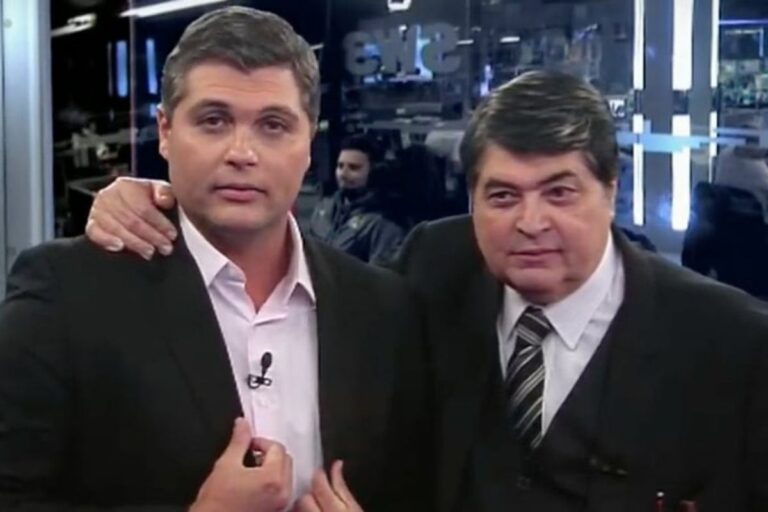 O jornalista e apresentador Joel Datena à esquerda, vestindo terno escuro e camisa clara, com o braço de seu pai, o também apresentador José Luiz Datena, apoiado em seu ombro. José Luiz Datena aparece à direita, sorrindo discretamente, vestindo terno escuro, colete e gravata listrada, em um cenário de estúdio de televisão.