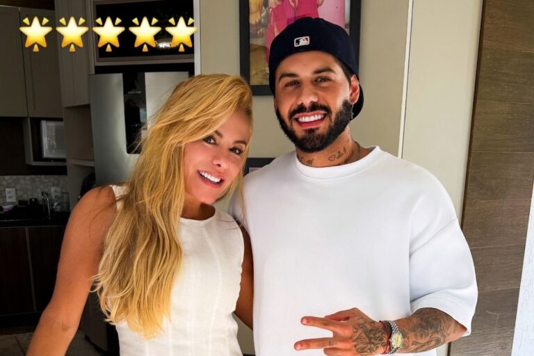 Poliana Rocha, mulher loira de cabelos longos, sorri ao lado de seu filho, o cantor Zé Felipe, que usa boné preto e camiseta branca. Eles estão em um ambiente interno com iluminação clara.