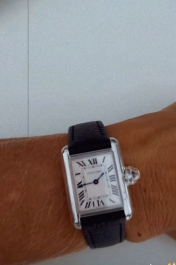 Pulso de Poliana Rocha exibindo um relógio de luxo da marca Cartier, com pulseira de couro preta e mostrador retangular clássico com algarismos romanos.