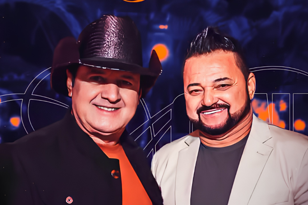 Os cantores Renan e Ray sorrindo lado a lado; Renan à esquerda usa um chapéu de cowboy preto e blazer escuro, e Ray à direita possui barba aparada e veste um blazer claro.