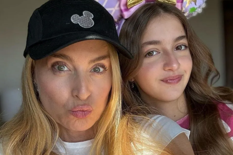 Angélica faz bico para a foto usando um boné preto com o símbolo do Mickey, enquanto sua filha Eva sorri discretamente ao lado usando uma tiara de orelhinhas da Minnie.