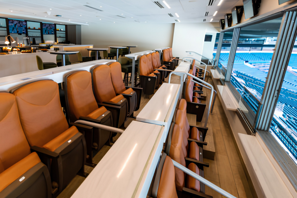 Interior de camarote luxuoso no Hard Rock Stadium com poltronas de couro marrom dispostas em fileiras e vista panorâmica para as arquibancadas do estádio.