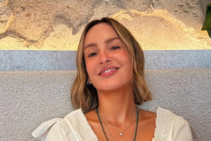 Cantora Claudia Leitte sorri de frente para a câmera. Ela tem cabelos loiros curtos no corte bob, usa blusa branca com decote e colares delicados.