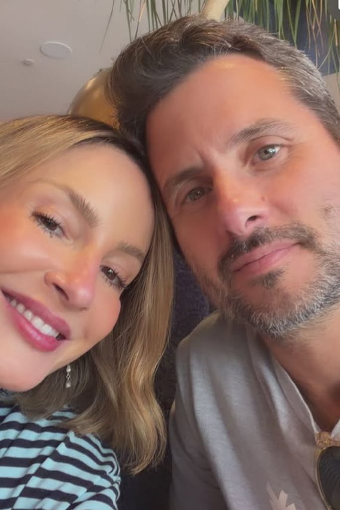 Close-up de Claudia Leitte sorrindo ao lado de seu marido, Márcio Pedreira, com as cabeças encostadas. Ela usa blusa listrada e ele, camiseta cinza.