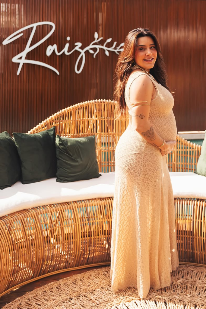 Lauana Prado exibe barriga de grávida ao usar vestido longo de tricô em ambiente externo com decoração rústica.