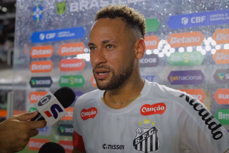 Neymar falando ao microfone da TV Globo durante entrevista na beira do gramado vestindo a camisa branca do Santos FC.