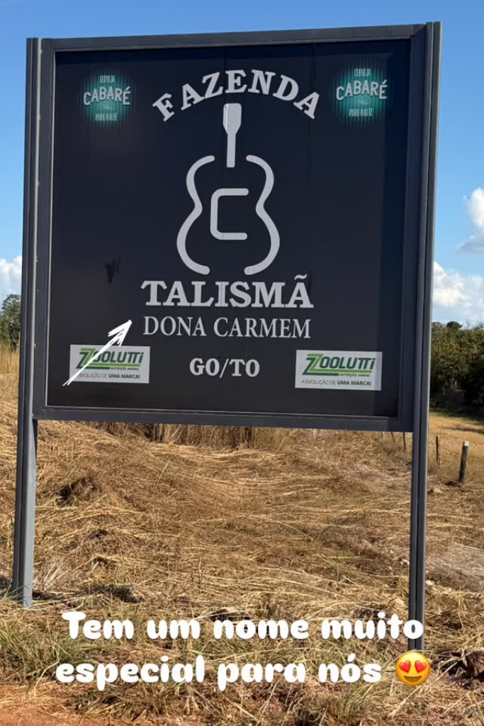 Placa informativa da Fazenda Talismã Dona Carmem com logotipos de patrocinadores em área rural.
