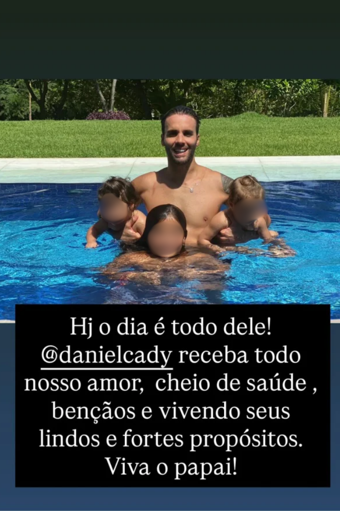 Captura de tela de publicação no Instagram de Ivete Sangalo. Na metade superior, Daniel Cady aparece sorridente em uma piscina com água azul clara, abraçado a três crianças que estão com os rostos borrados. Ao fundo, há um gramado verde e árvores. Na metade inferior, um texto em fundo preto diz: 