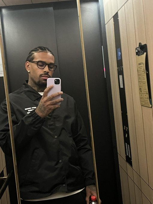 Jogador Jurgen Locadia com cabelo trançado, usando óculos de grau e jaqueta preta em selfie no espelho de um elevador.
