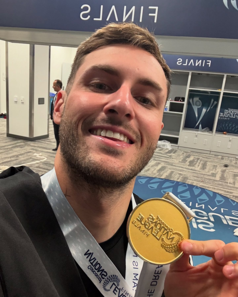 Jogador Santiago Gimenez sorrindo e segurando uma medalha de ouro da Concacaf Nations League no vestiário.