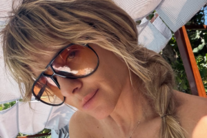 A atriz Carolina Dieckmann posa para uma selfie sob a sombra, usando óculos de sol grandes com lentes alaranjadas e o cabelo loiro preso em uma trança lateral.