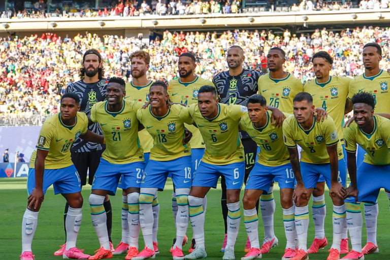 Foto oficial da Seleção Brasileira de futebol posada no gramado, com jogadores titulares e reservas perfilados vestindo o uniforme amarelo e azul, diante de arquibancada lotada.