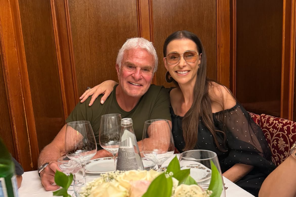 Mônica Martelli e Fernando Altério sorriem sentados lado a lado em um jantar, com ele vestindo verde e ela de preto.