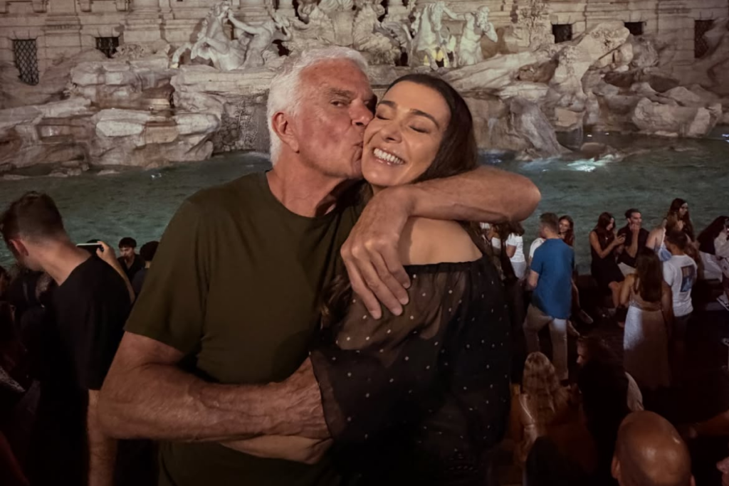 Fernando Altério beija o rosto de Mônica Martelli em pose carinhosa em frente à Fontana di Trevi à noite.