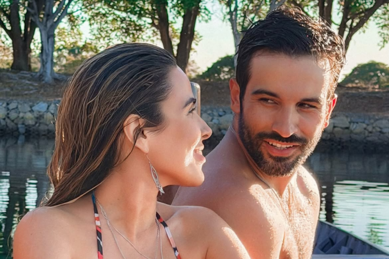 Wanessa Camargo e Bruno Bevan sorridentes, em momento de lazer ao ar livre próximo a uma área de água.
