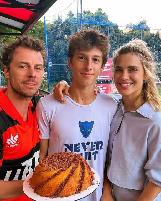 A atriz Carolina Dieckmann, seu marido Tiago Worcman e o filho José posam juntos em uma celebração segurando um bolo de aniversário com granulado.