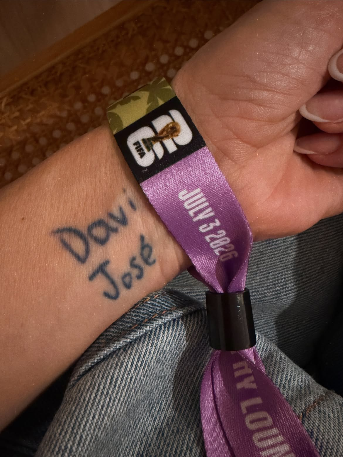 Pulso da atriz Carolina Dieckmann com uma tatuagem escrita à mão com os nomes Davi e José, acompanhada por uma pulseira de evento da Copa do Mundo FIFA com a data 3 de julho de 2026.