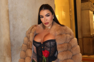 Influenciadora Kauana Bilhar veste casaco de pele bege e corset de renda preta, segurando uma rosa vermelha com as mãos tatuadas.