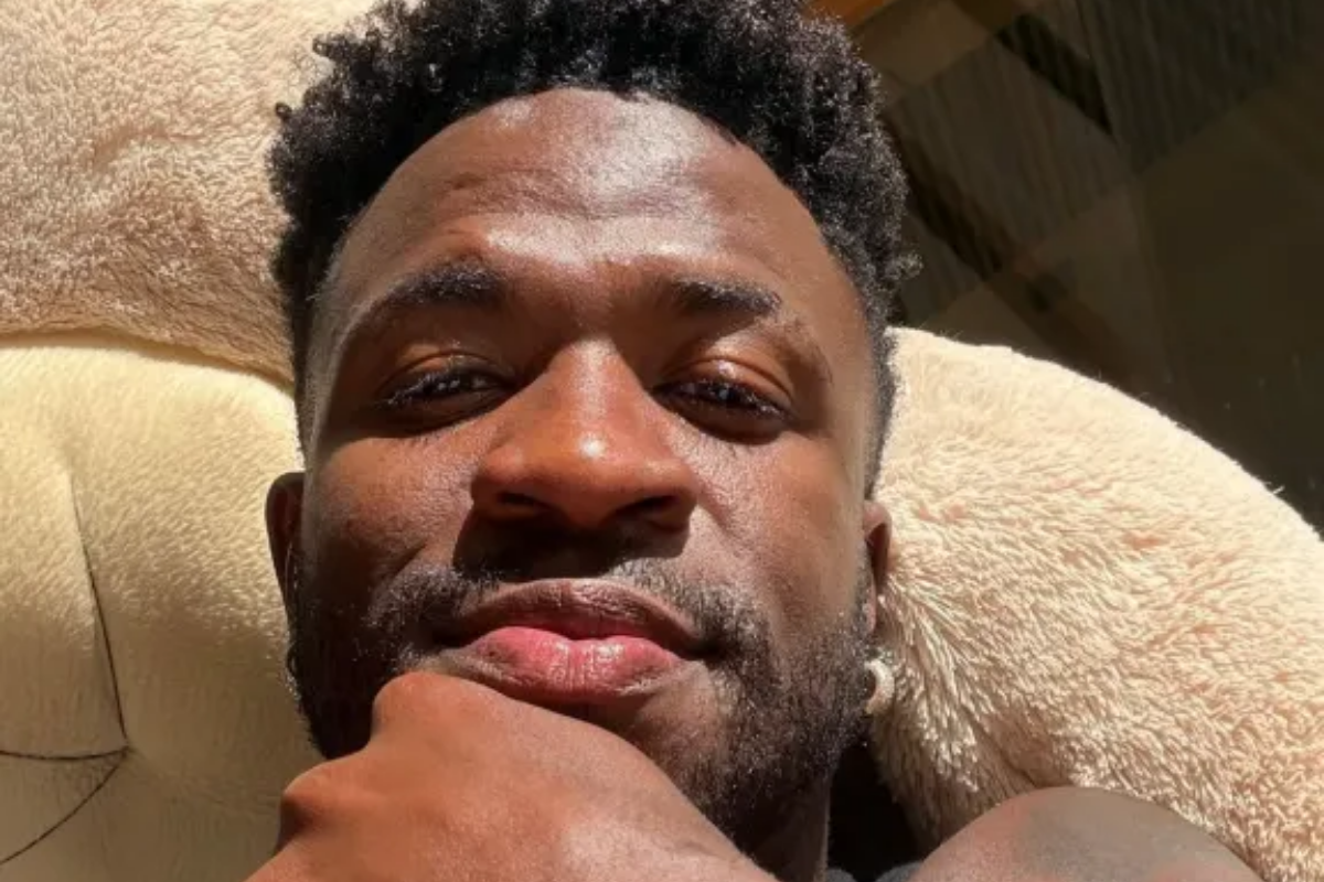 Vini Jr. sorri deitado com o queixo apoiado na mão em ambiente iluminado pelo sol