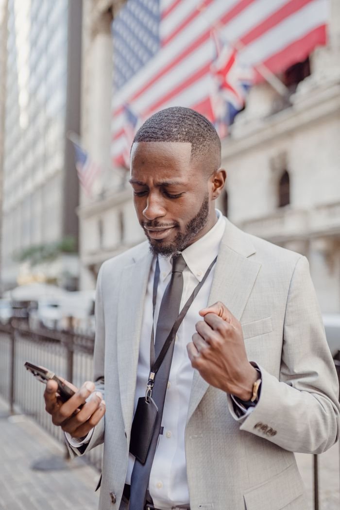 Confident businessman reading good news on his cellphone in front of a building with flags.